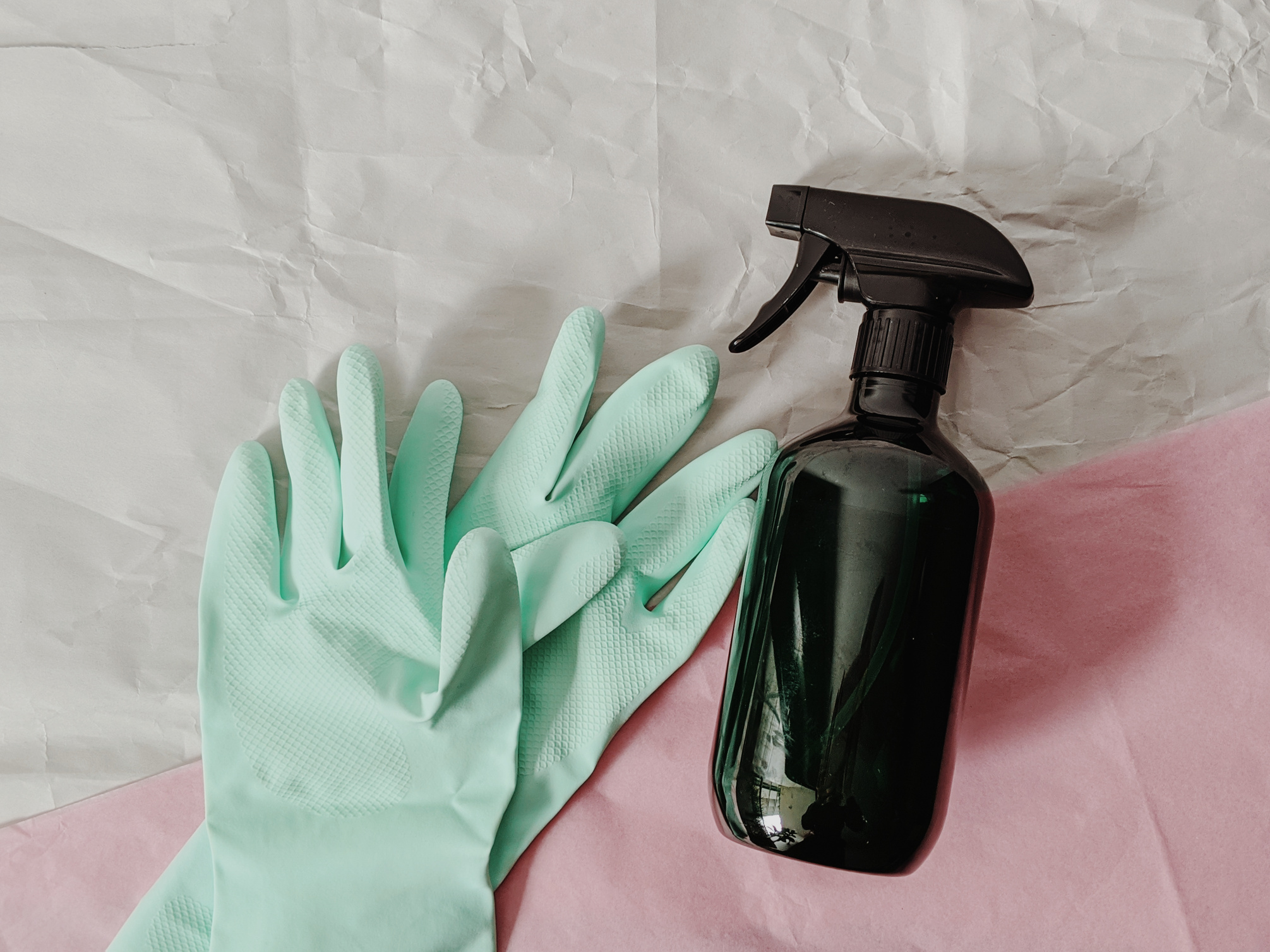 Rubber gloves and a spray bottle on pink and white background